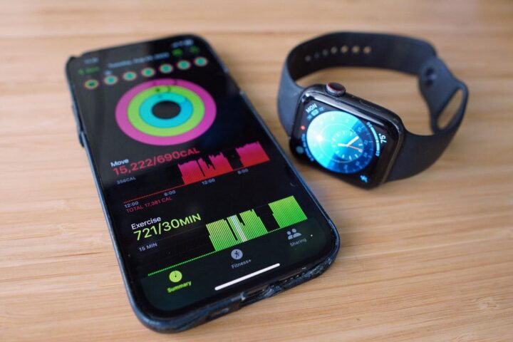 The Apple Watch Series 5 sits on a desk next to an iPhone with solid numbers written on it: a "move" 15,222 calories (at 690 calories per day) and 721 minutes of exercise (at 30 minutes goal per day).